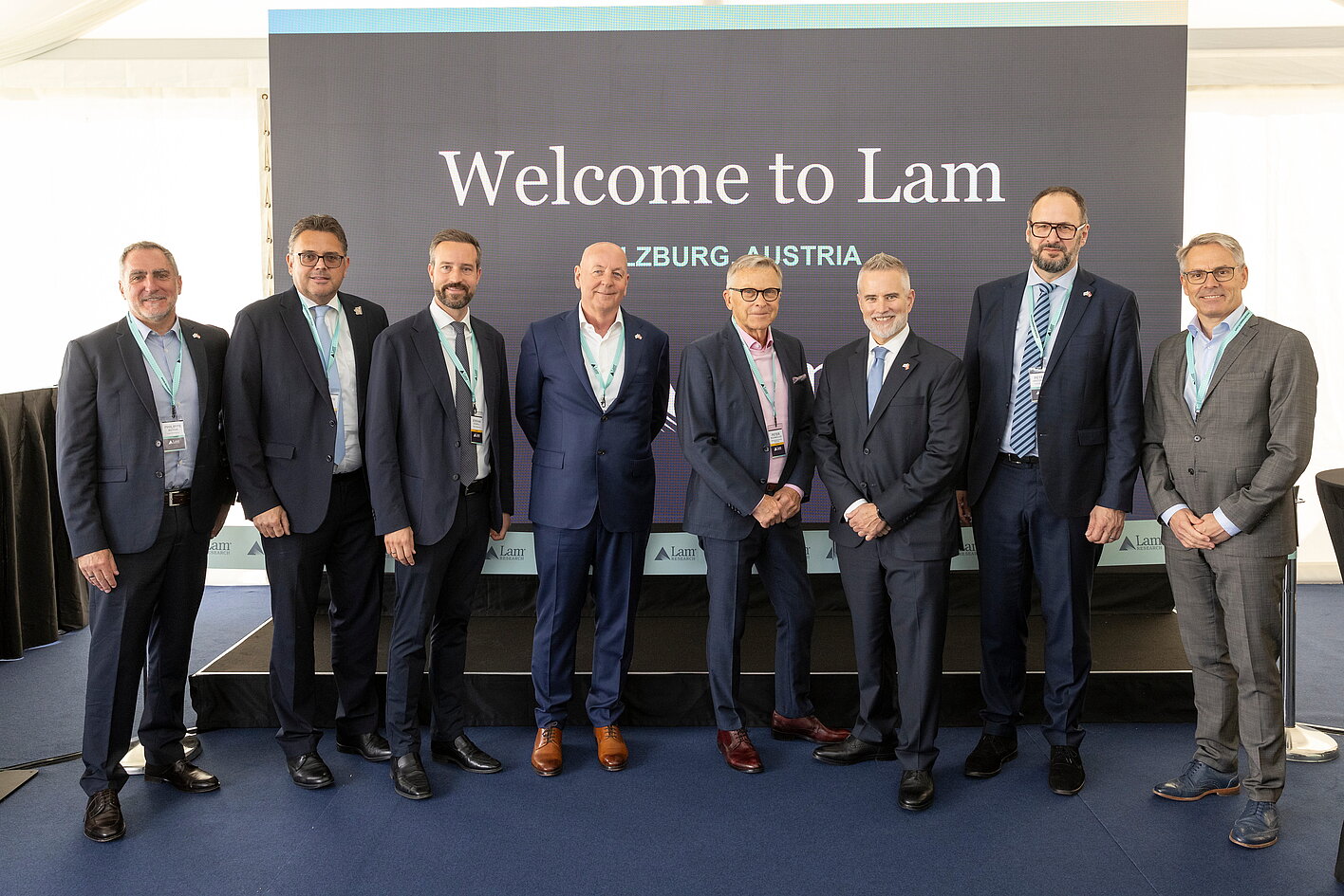 Group photo at Lam Research opening in Salzburg with international guests in front of stage presenting semiconductor center