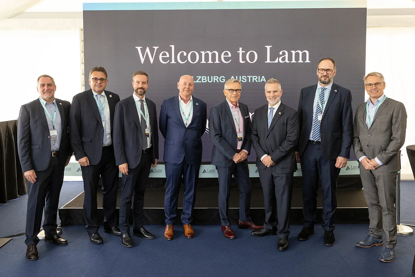 Group photo at Lam Research opening in Salzburg with international guests in front of stage presenting semiconductor center