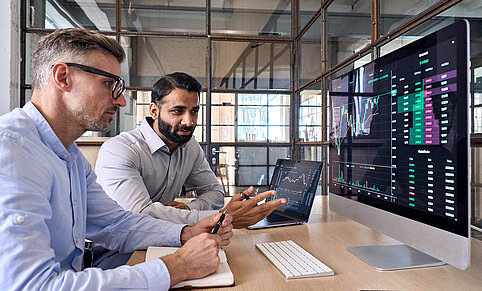 Zwei Krypto-Broker vor dem Bildschirm: Österreich bietet internationalen Unternehmen mit klarer Regulierung und Rechtssicherheit ein verlässliches Umfeld für digitale Finanzinnovationen.